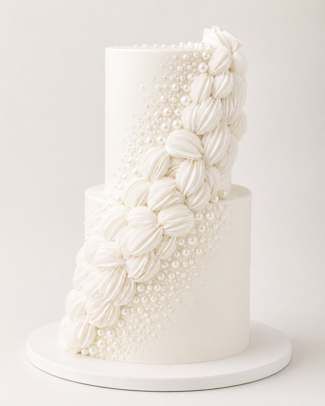 The Petal Cascade Cake, a luxury white statement cake with sculpted petal cascade detailing and delicate pearl-style accents on a white cake board.